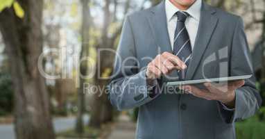 Businessman holding tablet on path with trees