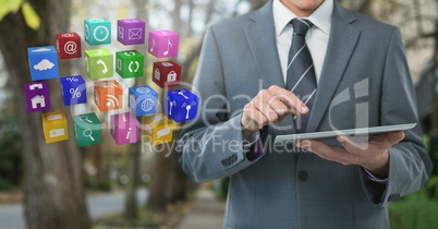 Businessman holding tablet with apps icons on path with trees