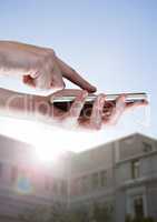 Hands touching phone against blurry building with flare