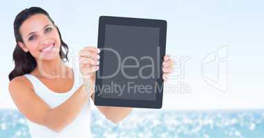 Smiling woman holding out tablet against blurry water on sunny day