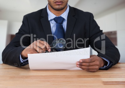 Man looking at paper with magnifying glass at desk