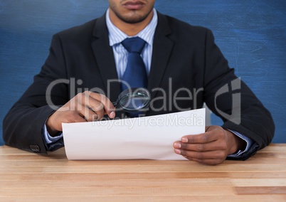 Man looking at paper with magnifying glass at desk