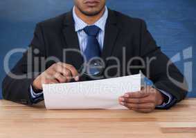 Man looking at paper with magnifying glass at desk