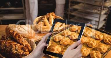 Cropped hand photographing breads in tray on table through digital tablet at bakery
