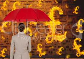 Digital composite image of businesswoman holding red umbrella looking at burning symbol of pounds