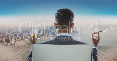 Rear view of businessman sitting on chair with glass of alcohol and smoking cigar while looking at c