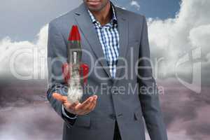 A model wearing a suit is holding a rocket taking off from his hand on sky background