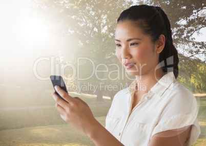 Woman looking at phone against blurry park and flare