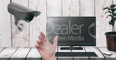 Hand holding glass screen with Security camera watching laptop