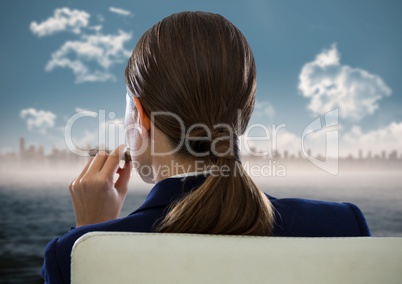Back of seated business woman smoking cigar and looking at blurry skyline and water