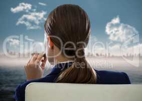 Back of seated business woman smoking cigar and looking at blurry skyline and water