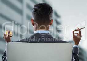 Back of seated business man smoking cigar and drinking while looking at blurry building