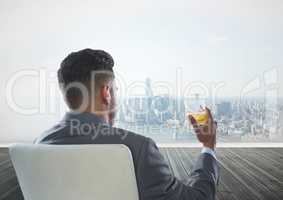 Rear view of businessman sitting on chair holding glass of alcohol while looking at city