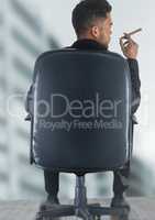 Back of seated business man smoking cigar against wood floor and blurry building
