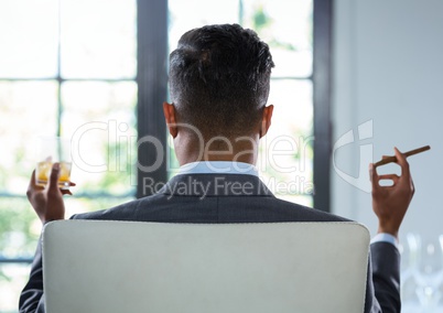 Businessman Back Sitting in Chair with cigar and drinks glass by window