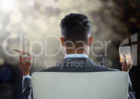 Businessman Back Sitting in Chair with cigar and drink glass with bokeh sparkling lights