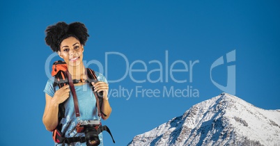 Portrait of happy hipster carrying backpack and camera standing against mountain