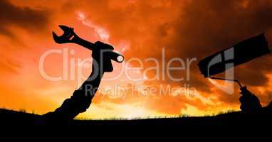 Silhouette hands holding tools against sky during sunset