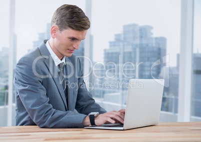 Businessman on laptop against windows with city