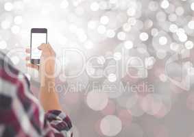 Hand holding mobile phone with sparkling light bokeh background
