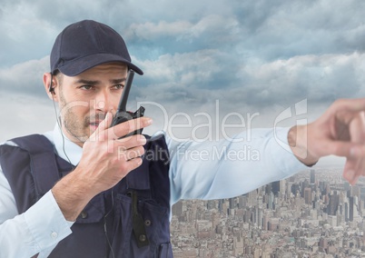 Security guard with walkie talkie pointing against skyline and clouds