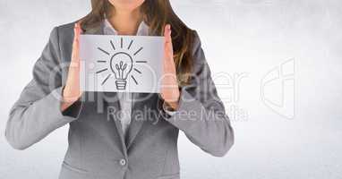 Business woman mid section with card showing grey lightbulb graphic against white wall