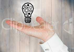 Hand with cogs in lightbulb graphic and flare against grey wood panel