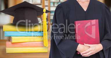 Mid section of female graduate holding red diary while standing by mortar board and stack of books