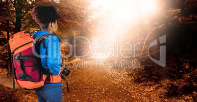 Rear view of hipster carrying backpack and holding camera while standing in forest