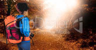 Rear view of hipster carrying backpack and holding camera while standing in forest