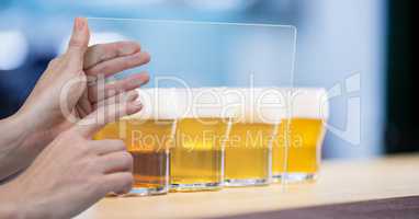 Cropped hands taking picture of beer glasses through transparent device at bar