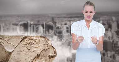 Digital image of angry businesswoman standing by rock against city