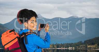 Hipster carrying backpack taking picture through smart phone standing on road against mountains