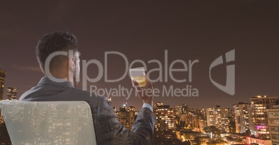 Rear view of businessman sitting on chair holding glass of alcohol and looking at city