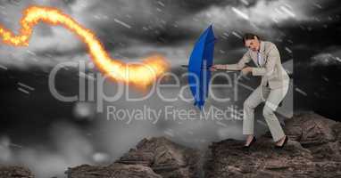 Digital composite image of businesswoman standing on rock holding blue umbrella against fire during