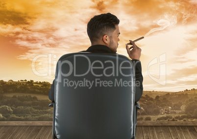 Businessman sitting on chair and smoking cigar against sky