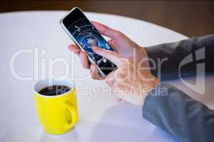Hands showing the screen of a smartphone next to a cup of coffee against desk background