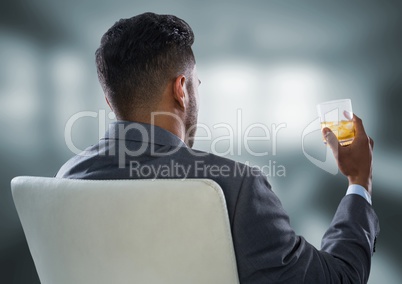 Back of seated business man drinking in blurry grey office