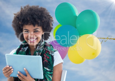 Woman with tablet against sunny sky and balloons