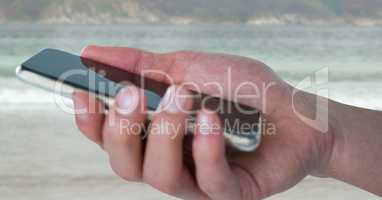 Hand with phone against blurry beach