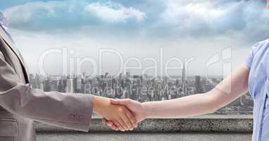 Cropped image of businessman and businesswoman shaking hands against city