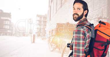 Hipster carrying backpack with camera standing against buildings
