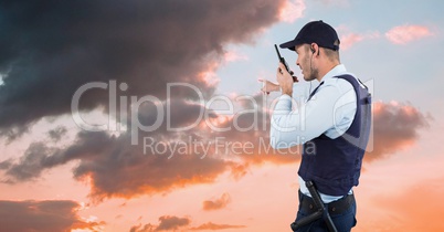 Security guard gesturing and talking on walkie talkie while facing towards sky