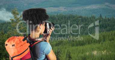 Hipster carrying backpack and photographing with camera while standing on cliff