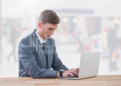 Businessman on laptop in bright shopping mall