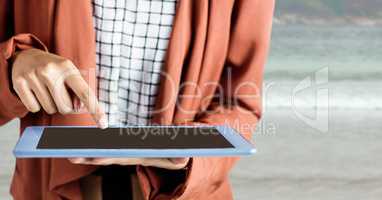 Woman orange coat mid section with tablet against blurry beach