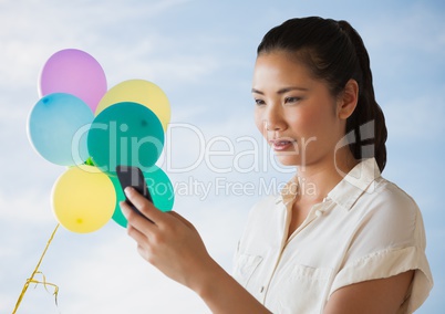 Woman looking at phone against sky and balloons