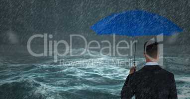 Back of business man with umbrella against stormy sea with rain