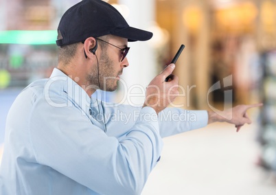 Security guard with walkie talkie pointing against blurry shopping centre