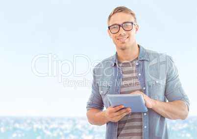 Man with tablet against blurry water on sunny day